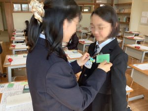 上級生が、新入生にコサージュ代わりに毛糸の人形をつけている様子